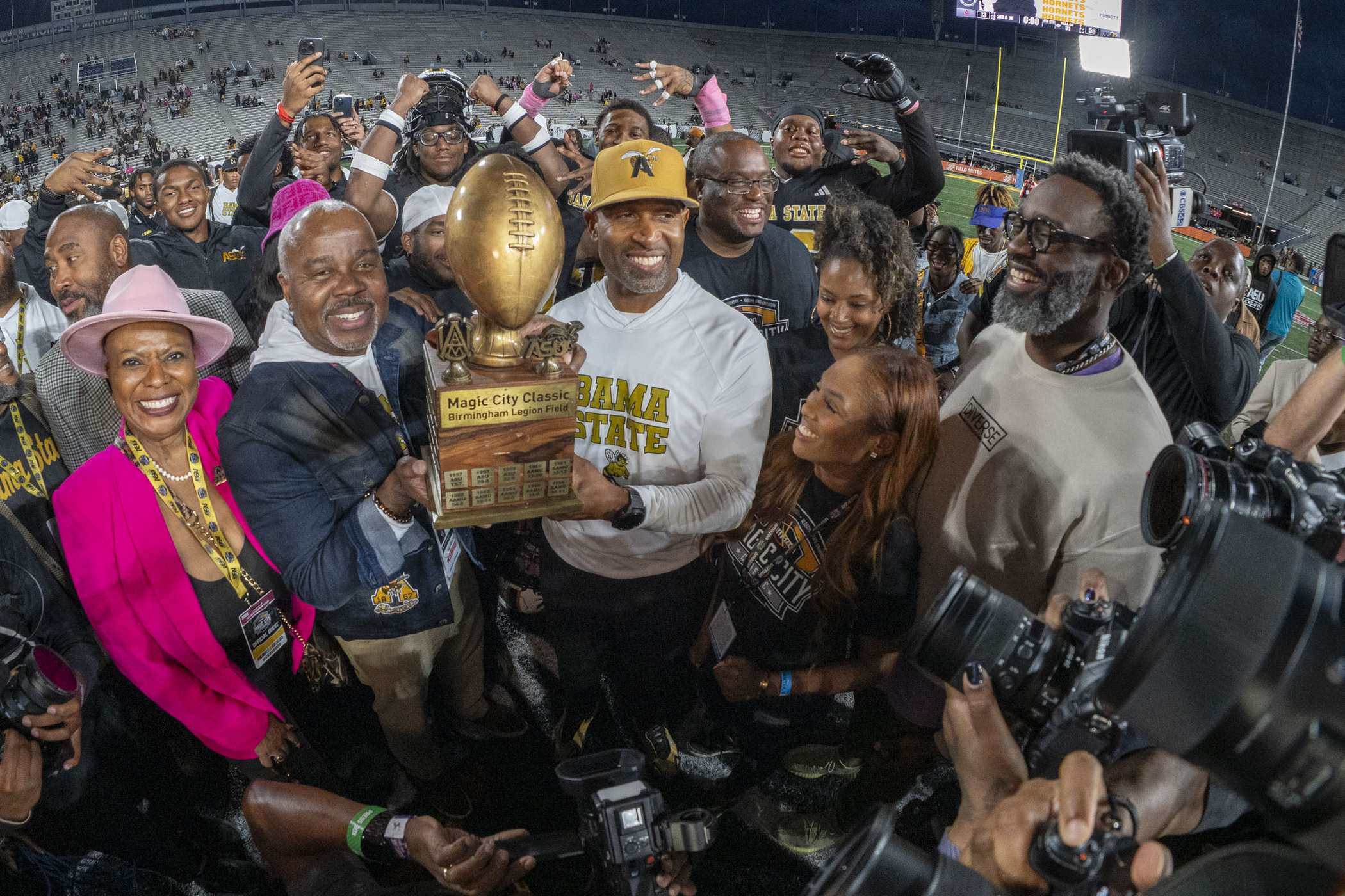 ASU staff and football players holding a trophy on the field. 